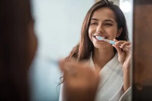 Young woman brushing teeth with a mirror.