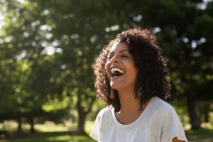 Happy woman laughing in a sunny park, showcasing the positive connection between oral care and general well-being.